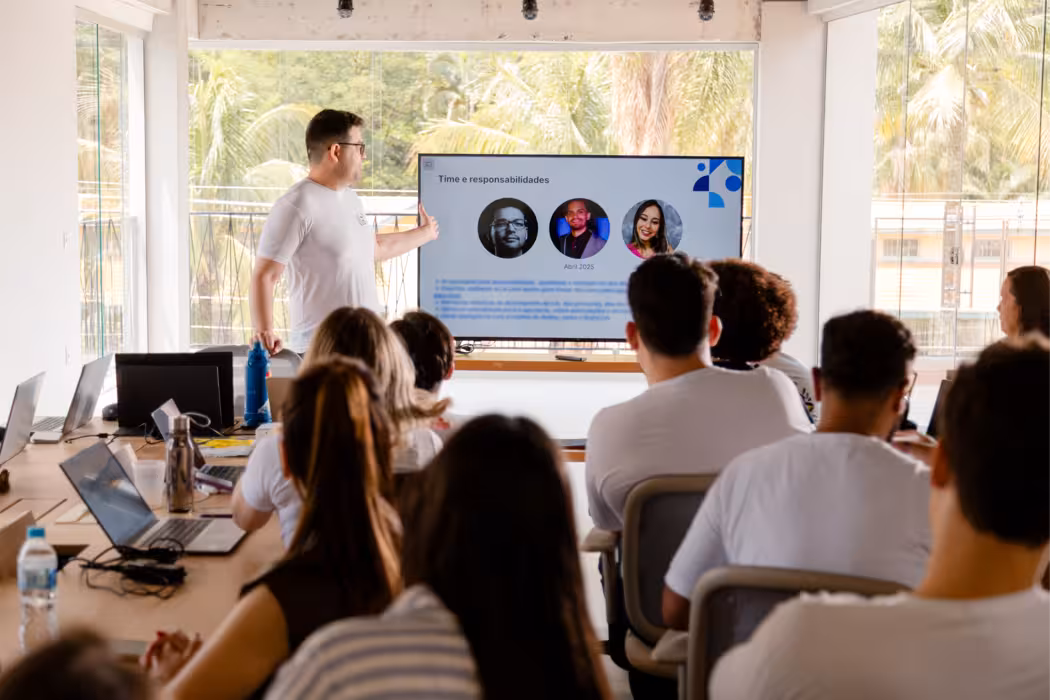 Time da Lia reunido presencialmente, a foto mostra os integrantes do time sentados de frente para um outro integrante do time enquanto faz uma apresentação